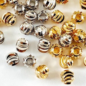 Könnte beinhalten: Nahaufnahme verschiedener Metallperlen in Gold und Silber. Die Perlen haben ein geripptes, zylindrisches Design, einige weisen eine sternartige Form auf. Die glänzenden Perlen sind über die Oberfläche verstreut und reflektieren das Licht.