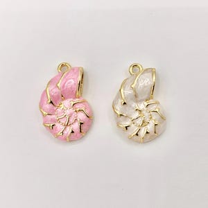 May include: Two seashell-shaped pendants. One is pink with gold trim, the other is white with gold trim. Both have a loop at the top for hanging. The pendants are likely for jewelry making or crafting.