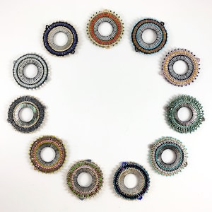 May include: Twelve beaded rings in various colors and patterns, arranged in a circle on a white background.