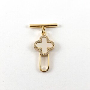 May include: Gold-tone metal toggle clasp with a white enamel four-leaf clover charm. The clover has a gold-tone metal border and is embellished with clear rhinestones.