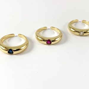 May include: Three gold rings with different colored gemstones. The rings are simple and have a rounded band. The gemstones are a blue sapphire, a red ruby, and a clear diamond.