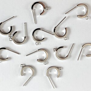 May include: A group of silver earring hoops with a post and a loop. The hoops are all the same size and shape.