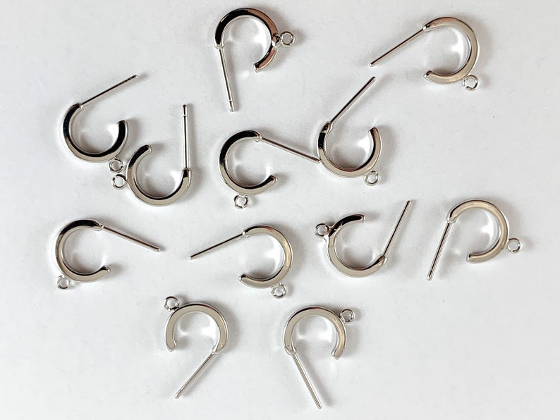 May include: A group of silver earring hoops with a post and a loop. The hoops are all the same size and shape.