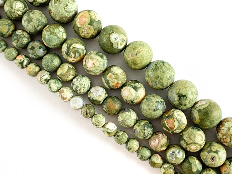 May include: A strand of green, brown and white patterned round gemstone beads. The beads are various sizes and are strung together on a white background.