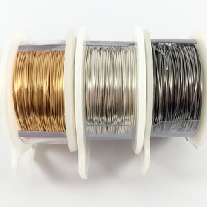 K&ouml;nnte beinhalten: Drei Spulen Draht, eine gold, eine silber und eine schwarz, liegen auf einer wei&szlig;en Oberfl&auml;che.