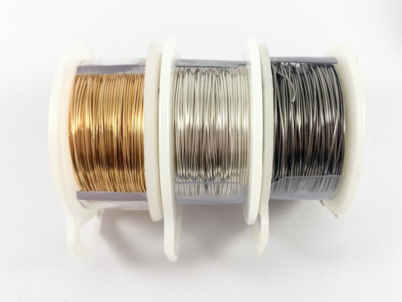 K&ouml;nnte beinhalten: Drei Spulen Draht, eine gold, eine silber und eine schwarz, liegen auf einer wei&szlig;en Oberfl&auml;che.