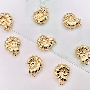 May include: Ten gold-colored metal charms shaped like seashells. Each charm has a hole at the top for attaching to a necklace, bracelet, or other jewelry.