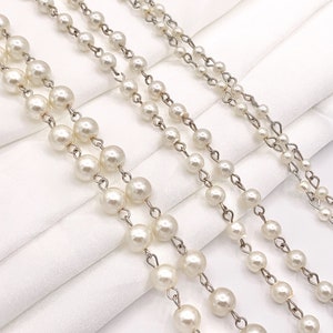 May include: Three strands of faux pearl necklaces with silver chain links. The necklaces are laid out on a white fabric background.