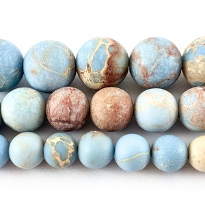 May include: A strand of blue, brown, and cream marbled jasper beads. The beads are round and have a smooth, polished finish.