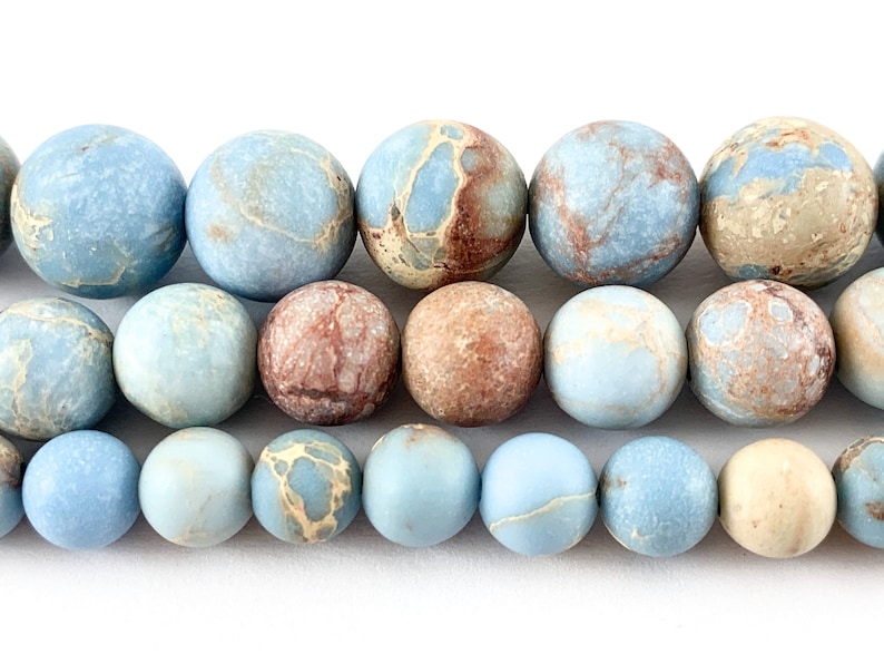 May include: A strand of blue, brown, and cream marbled jasper beads. The beads are round and have a smooth, polished finish.