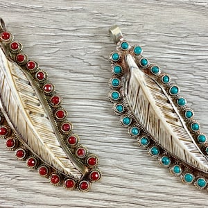 May include: Two silver feather pendants with a carved bone design. One pendant is decorated with red stones and the other with turquoise stones.