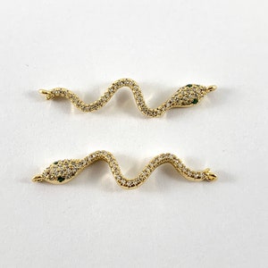 May include: Two gold snake charm connectors with clear and green rhinestones. The snake charms are in a curled position with their heads facing opposite directions.