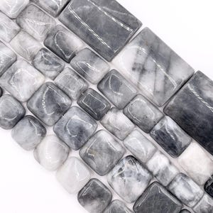 May include: Close-up of a collection of gray and white rectangular and square beads. The beads have a polished, glossy finish and a marbled appearance. The beads are arranged diagonally against a white background.