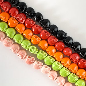 May include: A strand of colorful skull beads in shades of pink, green, orange, red, and black. The beads are made of ceramic and have a glossy finish.