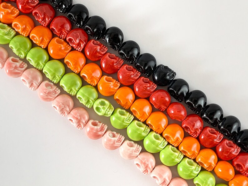May include: A strand of colorful skull beads in shades of pink, green, orange, red, and black. The beads are made of ceramic and have a glossy finish.
