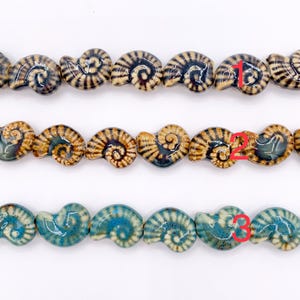 May include: Three horizontal strands of ceramic beads shaped like ammonite fossils. The top row features tan and dark brown stripes, the middle row displays brown and blue-green tones, and the bottom row consists of bright turquoise and cream beads.