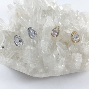 May include: Three pairs of teardrop-shaped earrings with clear cubic zirconia stones. The earrings are set in silver, gold, and rose gold.