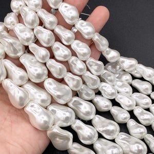 May include: A strand of white pearl-like beads, each bead is shaped like a teardrop. The beads are strung together on a clear thread and are arranged in a cascading pattern.
