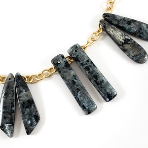 May include: A gold chain necklace with five dangling, dark gray, rectangular and teardrop-shaped stones.
