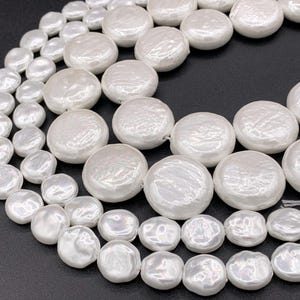 May include: A strand of white pearl beads with a mix of round and irregular shapes. The beads are strung on a white thread and are arranged in a loose, flowing pattern.