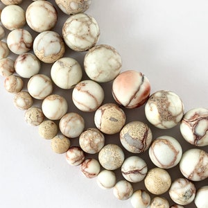 May include: A strand of white, brown, and beige jasper beads with a marbled pattern. The beads are round and smooth, and they are arranged in a graduated size from smallest to largest.