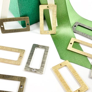 May include: Assortment of metal label holders in various finishes, including gold, silver, and bronze. The label holders are rectangular with a textured surface and have a hole at the top for hanging.