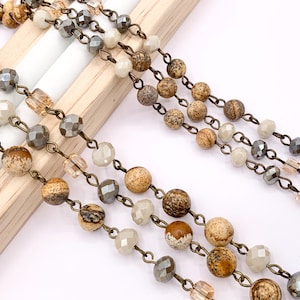 May include: A close-up of a multi-strand necklace with brown, beige, and gray beads. The beads are strung on a bronze chain.