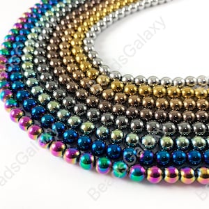 May include: A close-up of a strand of iridescent round beads in various colors, including blue, green, gold, and silver. The beads are arranged in a circular pattern, with the colors gradually transitioning from one to the next.