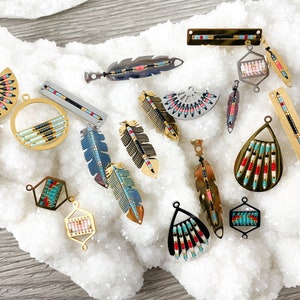 May include: Assortment of gold and silver tone metal bead and feather charms with geometric and fan shapes. The charms are arranged on a white background.