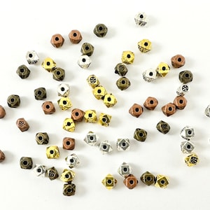 May include: A collection of small, metal, geometric beads in silver, gold, and copper tones. The beads are shaped like cubes with a small hole in the center.