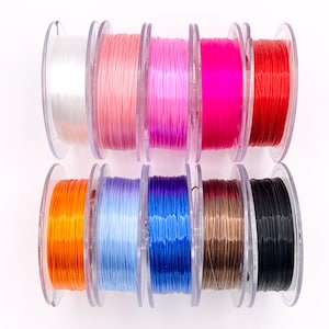 May include: A collection of colorful elastic string spools in various shades, including white, pink, orange, blue, and black. The spools are transparent, and the string is tightly wound. Ideal for crafting and jewelry making.
