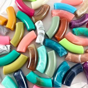May include: A collection of curved beads in various colors, including pink, green, blue, and brown. Some beads have a marbled effect. These beads are likely for jewelry making or other craft projects.