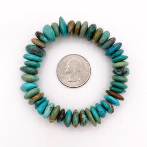 May include: A turquoise stone bracelet with a variety of blue-green hues. The bracelet is circular and made of polished, irregular-shaped stones. A US quarter is next to the bracelet for size reference.