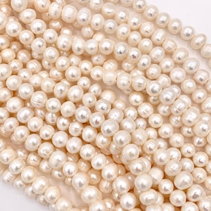 May include: A close-up view of numerous creamy white pearls. The pearls are of varying sizes and shapes, strung together, creating a textured and lustrous appearance. The overall composition suggests a jewelry-making supply or a finished necklace.