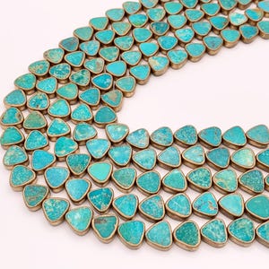 May include: Rows of turquoise-colored, triangular stones with gold-colored metal edging. The stones are arranged in a curved pattern against a white background. The turquoise stones have a mottled appearance, with variations in color.