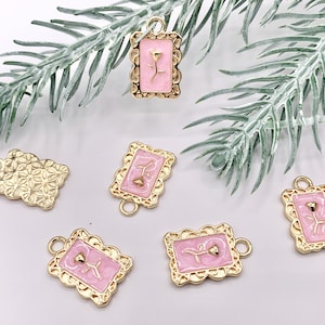 May include: Six gold-tone charms with pink enamel and a floral design. The charms are rectangular and have a scalloped edge. Each charm has a small loop at the top for attaching to a necklace or bracelet.