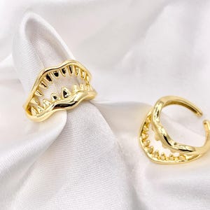 May include: Two gold-tone rings shaped like a set of teeth. The rings are open and have a wavy design.
