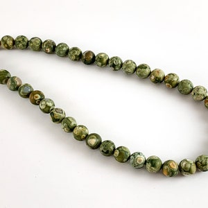 May include: A strand of green, brown and white patterned gemstone beads. The beads are round and have a smooth, polished finish.