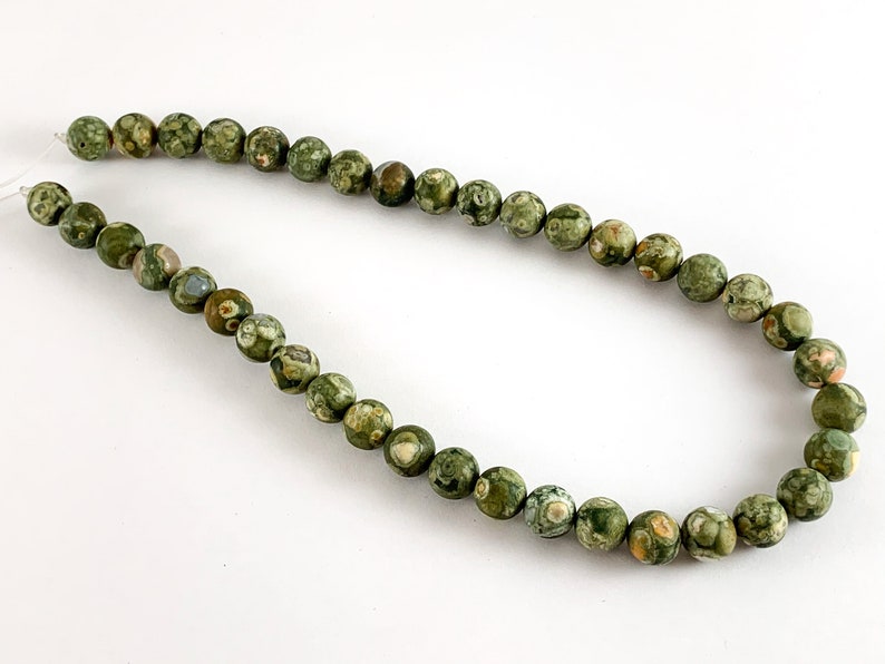 May include: A strand of green, brown and white patterned gemstone beads. The beads are round and have a smooth, polished finish.