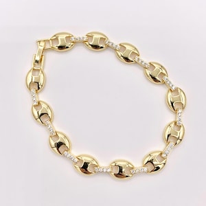 May include: A gold-colored bracelet featuring a series of oval-shaped links. Each link is connected by smaller, rectangular links adorned with small, clear gemstones. The bracelet has a secure clasp for easy wear.