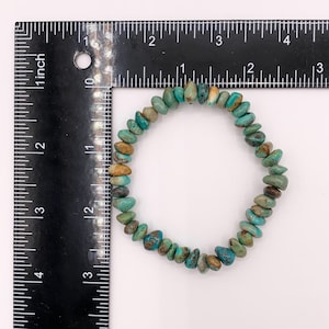 Pu&ograve; includere: Un braccialetto di schegge di turchese con un mix di pietre blu, verdi e marroni. Il braccialetto ha una circonferenza di circa 18 cm. Le pietre sono di forma irregolare e infilate su un elastico. Un righello &egrave; accanto.