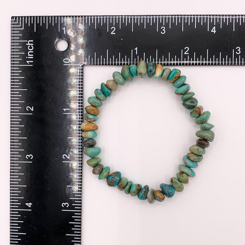 Pu&ograve; includere: Un braccialetto di schegge di turchese con un mix di pietre blu, verdi e marroni. Il braccialetto ha una circonferenza di circa 18 cm. Le pietre sono di forma irregolare e infilate su un elastico. Un righello &egrave; accanto.