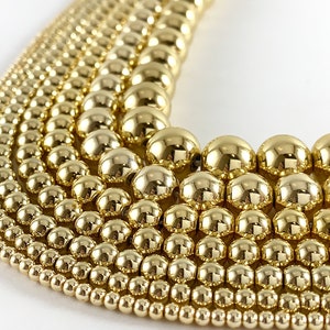 May include: A close-up of a variety of gold-toned round beads arranged in a fan shape. The beads are different sizes, creating a graduated effect.