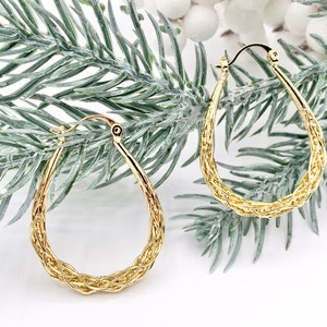 May include: A pair of gold-toned hoop earrings with a braided design. The earrings are oval-shaped and have a smooth finish.