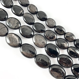 May include: A strand of black obsidian beads with a silver sheen. The beads are oval shaped and have a smooth, polished finish.