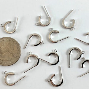 May include: A close-up of 11 silver earring hoops with a post and a loop. The hoops are about the size of a US quarter.