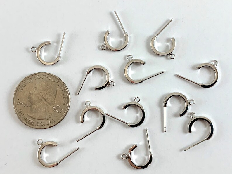 May include: A close-up of 11 silver earring hoops with a post and a loop. The hoops are about the size of a US quarter.