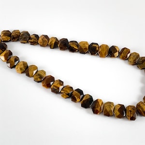 May include: A strand of brown and gold tiger's eye beads. The beads are faceted and have a geometric shape.