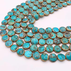 May include: Close-up of turquoise gemstone beads with a gold-colored metal rim. The beads are round and have a mottled appearance with shades of blue and brown. The beads are strung together, creating a necklace or bracelet.