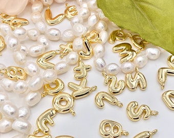 May include: A collection of gold-colored letter and number charms on a strand of white pearls. The charms are in various shapes and sizes, and some have a slightly raised design.